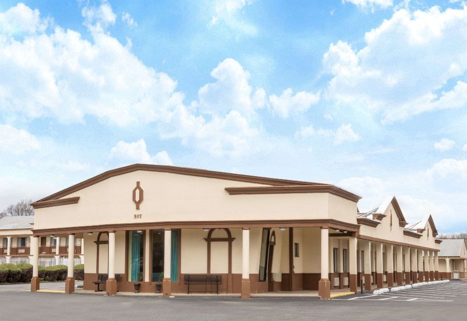 a large , beige building with a brown roof and pillars , standing under a blue sky dotted with clouds at Days Inn by Wyndham Wrightstown McGuire AFB/Bordentown