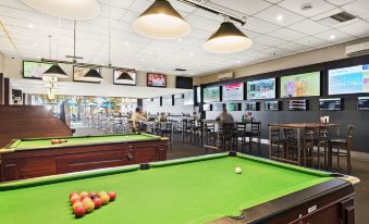 a game room with multiple pool tables , chairs , and tvs , as well as people playing games at North Pier Hotel