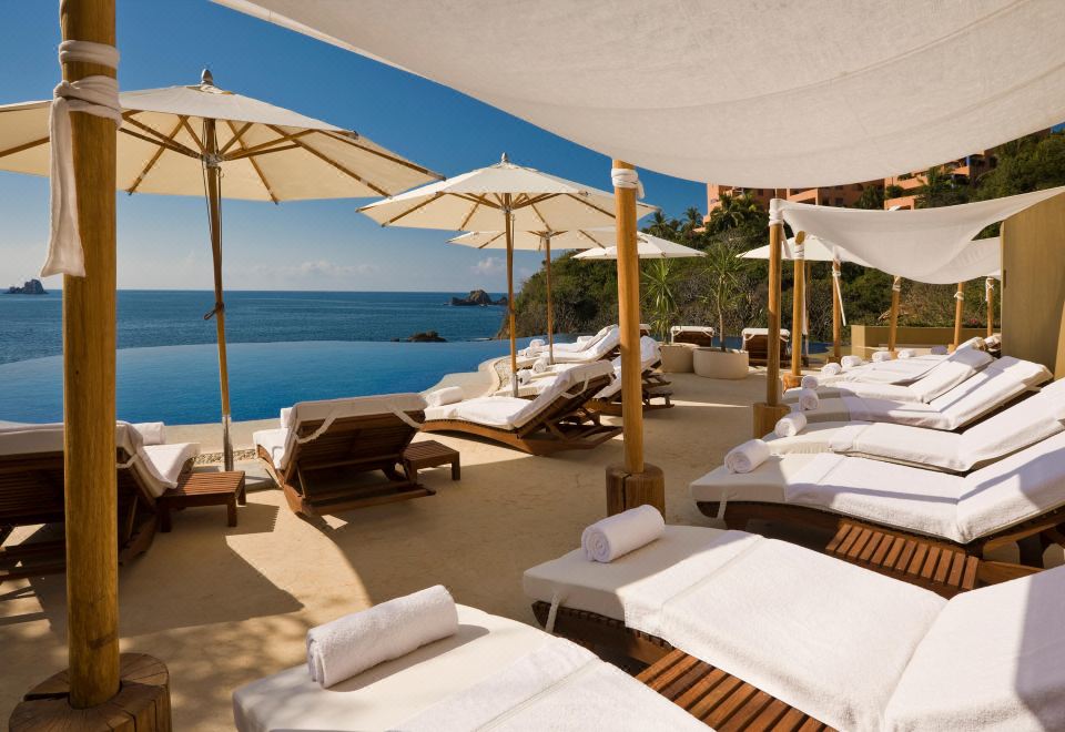 a large pool surrounded by lounge chairs and umbrellas , with a beautiful view of the ocean in the background at Cala de Mar Resort & Spa Ixtapa