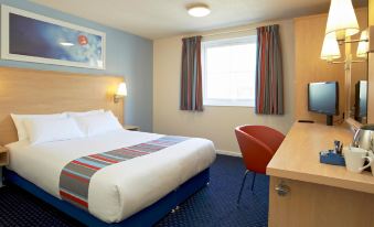 a hotel room with a blue and white bed , a chair , a television , and a desk at Travelodge Ipswich Beacon Hill