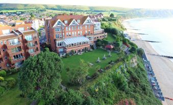 aerial view of a large brick building on a grassy hillside , surrounded by trees and overlooking the ocean at Grand Hotel Swanage