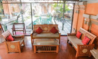 a living room with wooden furniture , including a couch and chairs , is shown with a view of a pool outside at Ubud Hotel & Cottages