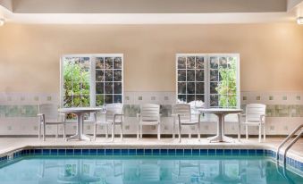 a pool area with a table and chairs , surrounded by large windows that offer views of the surrounding plants at Country Inn & Suites by Radisson, Kalamazoo, MI