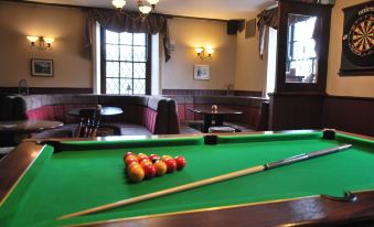 a pool table with a red ball and two pool balls , surrounded by chairs and tables in a restaurant at The Punchbowl Hotel