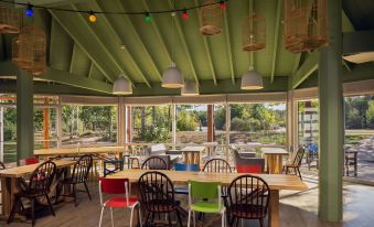 a modern , green - roofed restaurant with wooden tables and chairs , surrounded by trees and large windows at Center Parcs les Bois Francs