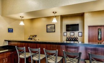 a well - lit bar area with several chairs and tables , along with a television mounted on the wall at Cobblestone Hotel & Suites - Erie