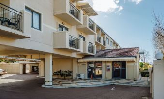 an apartment building with multiple balconies and a car parked in front , under a clear blue sky at Canning Bridge Auto Lodge