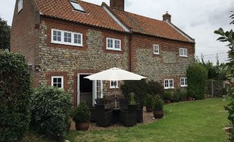 a brick house with a white umbrella in front of it , surrounded by green grass and bushes at Primrose Cottage