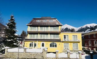 a yellow building with a brown roof and large windows is surrounded by snow - covered ground at Hotel Lindenhof