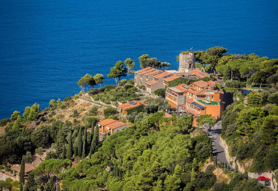 a picturesque village nestled on the edge of a cliff , with a body of water in the background at Boutique Hotel Torre di Cala Piccola