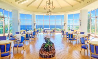 a large , round room with a wooden floor and walls has blue chairs and tables in the center at Kawana Hotel