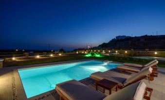 a large swimming pool with lounge chairs and a view of the ocean at night at Natura Villas in Naxos