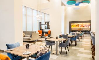 a modern restaurant with white walls , wooden tables , and chairs , blue upholstered chairs , and pendant lights at Holiday Inn Express Kolkata Airport