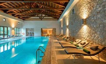 an indoor swimming pool surrounded by lounge chairs , with several people enjoying their time in the pool area at The Romanos, a Luxury Collection Resort, Costa Navarino
