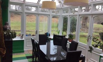 a modern glass dining room with a large table and black chairs , surrounded by windows at Bridge Cottage