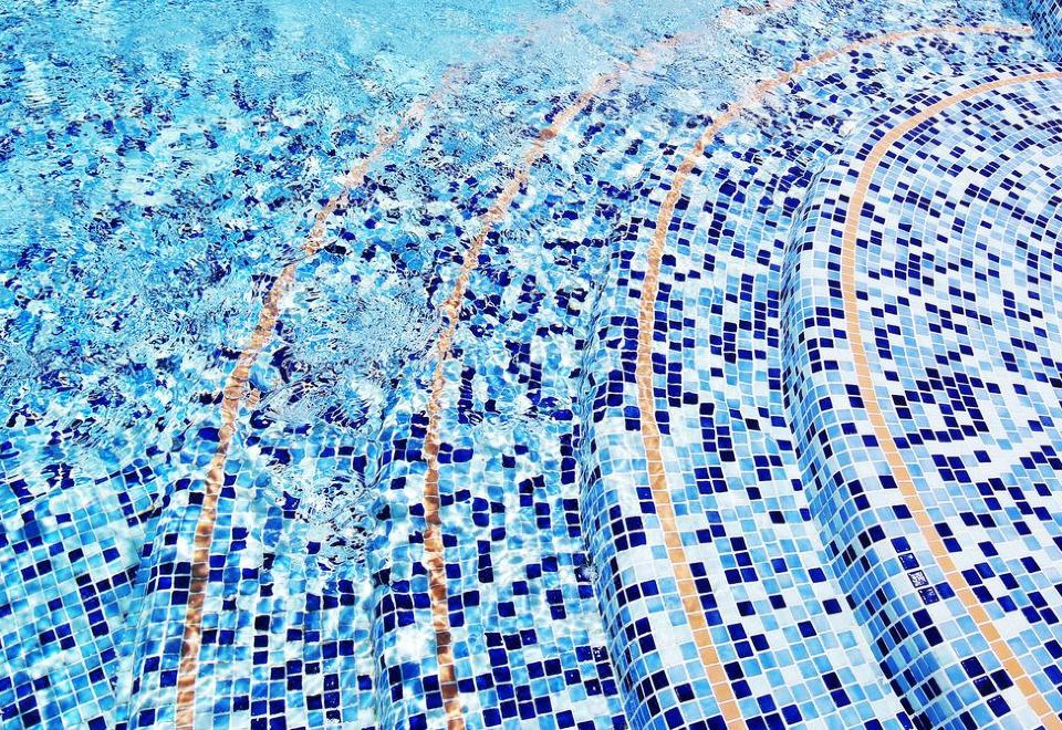 a close - up view of a swimming pool with blue mosaic tiles , water waves , and sunlight reflecting off the surface at Invisa Hotel la Cala