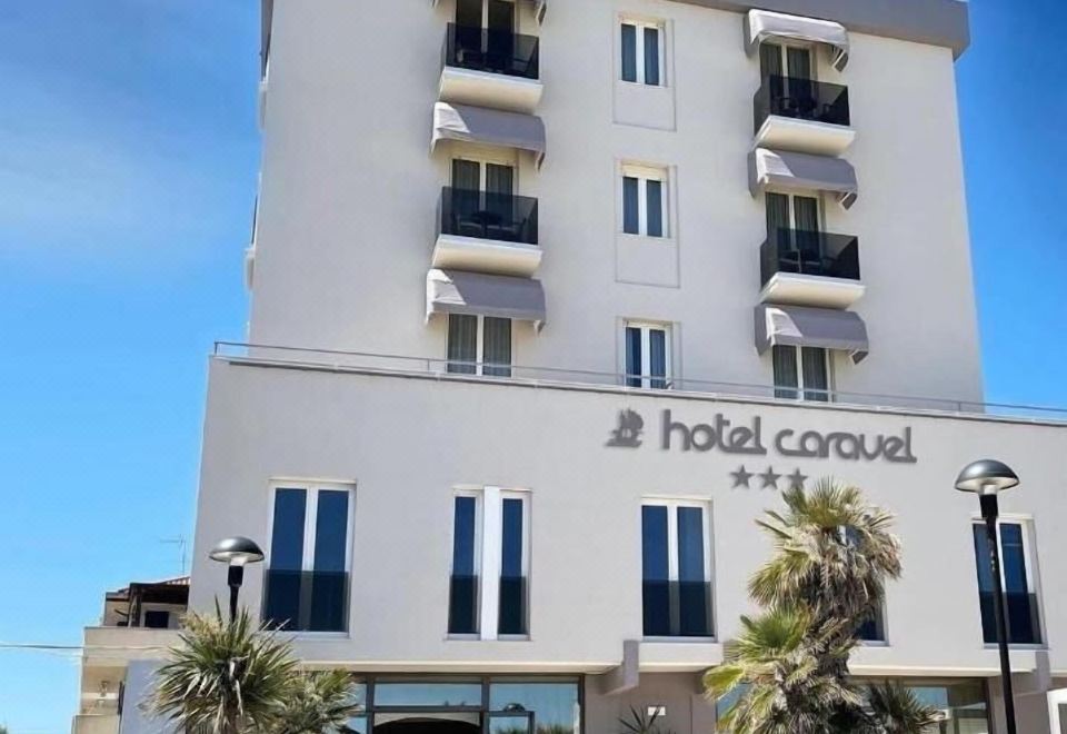 a large hotel building with a white exterior and multiple balconies , situated next to the ocean at Hotel Caravel