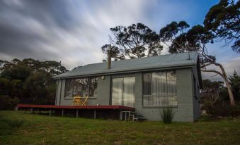a modern , green - roofed house with large windows and wooden decks , surrounded by trees and grass , under a cloudy sky at Bruny Island Escapes and Hotel Bruny