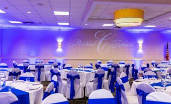 a well - decorated banquet hall with blue and white linens , chairs , and a large wall mural of the bride and groom at Holiday Inn Weirton - Steubenville Area