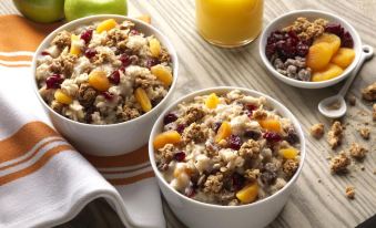 two bowls of cereal with fruit and nuts are placed on a table next to glasses of orange juice at Home2 Suites by Hilton Canton