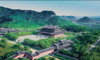 a traditional chinese building surrounded by lush greenery , with mountains in the background and a clear blue sky at Tam Coc Garden Resort