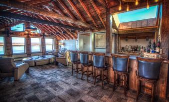 a large room with wooden walls and ceiling , featuring a bar area with stools and a pool table at The Cannery Lodge