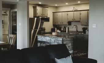 a modern kitchen with a stainless steel refrigerator and marble countertop , black chairs , and a black couch in the foreground at Riverside Suites