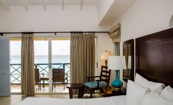 a hotel room with a balcony overlooking the ocean , featuring a bed , a chair , and a table at Infinity on the Beach