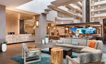 a modern hotel lobby with a large flat - screen tv mounted on the wall , along with various seating options for guests at Embassy Suites by Hilton Monterey Bay Seaside