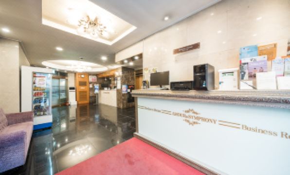 a reception area with a white desk , a red carpet , and a chandelier hanging from the ceiling at Symphony Hotel