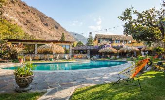 a large swimming pool surrounded by grass , with several lounge chairs and umbrellas placed around the pool area at Selina Atitlan
