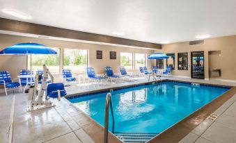 an indoor swimming pool with a large window , blue lounge chairs , and an umbrella on the side at Comfort Inn & Suites North Aurora - Naperville