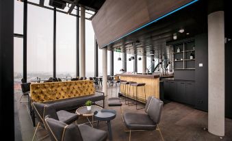 a modern bar with a large window , gray couches , and wooden stools , surrounded by windows offering views of the city at Arte Hotel Salzburg