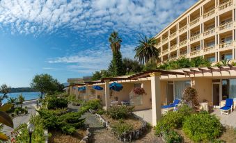 a beach resort with multiple buildings , umbrellas , and palm trees under a blue sky dotted with clouds at Corfu Palace Hotel