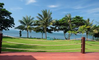 a beautiful tropical beach scene with palm trees , grassy dunes , and a blue sky , captured from a wooden deck at Lomtalay Resort Trat