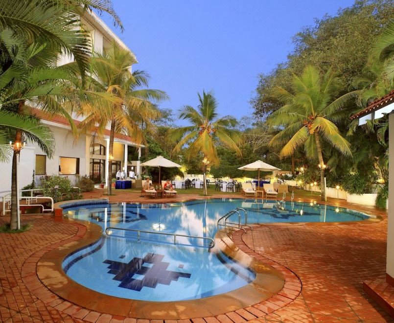 a large swimming pool with a fountain in the center is surrounded by palm trees and lounge chairs at Sangam Hotel, Thanjavur