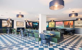 a modern restaurant with blue and white checkered floor , blue tables , green chairs , and large screens on the wall at Vila Gale Nautico