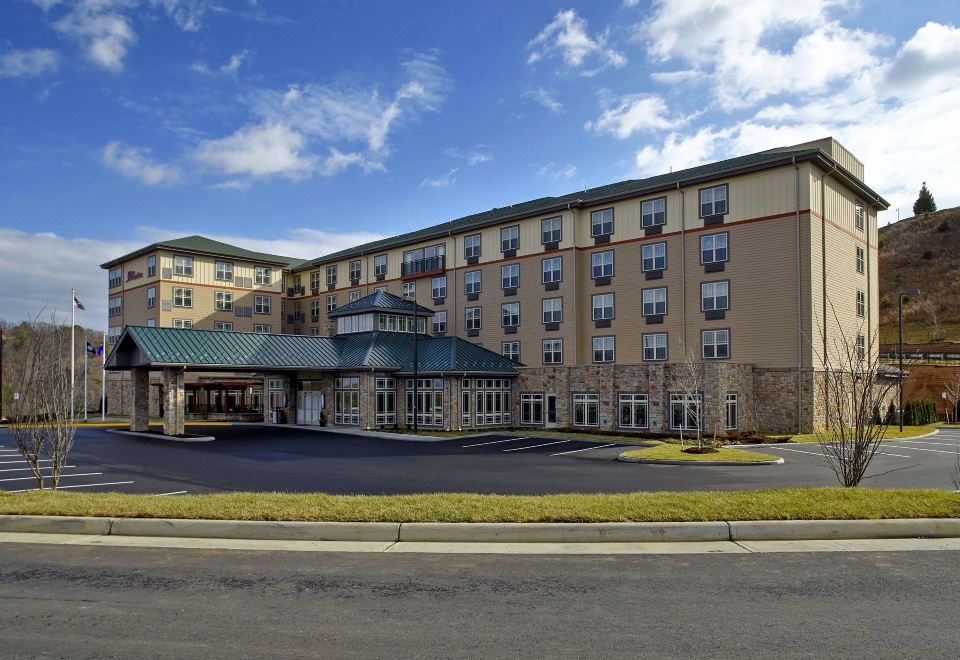 a large hotel building with a stone facade and a green roof is surrounded by trees at HIlton Garden Inn Roanoke