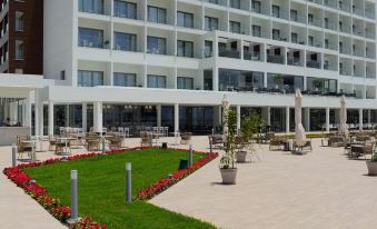 a large white hotel building with a green lawn and flowers in front of it at Ivi Mare - Designed for Adults by Louis Hotels