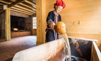 an older woman wearing a red hat is pouring water into a large pot on a wooden stove at Topas Riverside Lodge