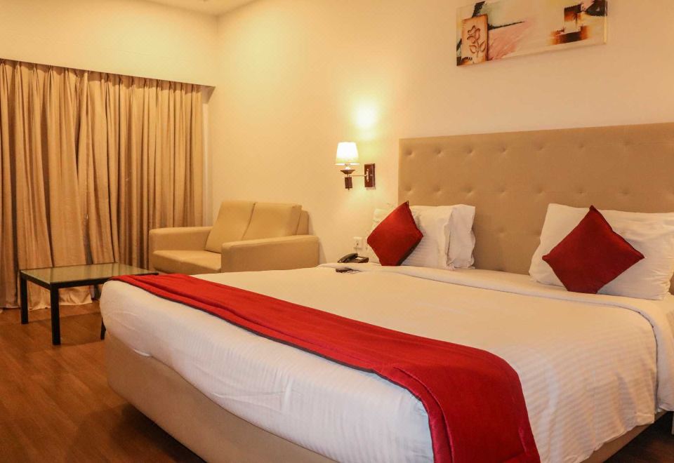 a large bed with a red blanket and white sheets is in a room with a couch and lamp at Hotel Midcity