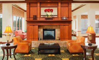 a cozy living room with a fireplace , two orange armchairs , and a wooden coffee table at Hilton Garden Inn Omaha West