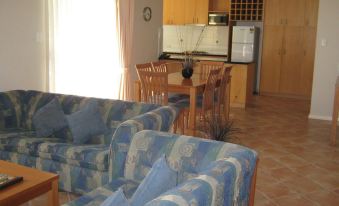 a living room with blue and white striped couches , a dining table , and a kitchen in the background at C Mandurah Apartment Resort