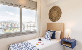 a bedroom with a large window , blue and white bed linens , and a blue nightstand at Pierre & Vacances Blanes Playa