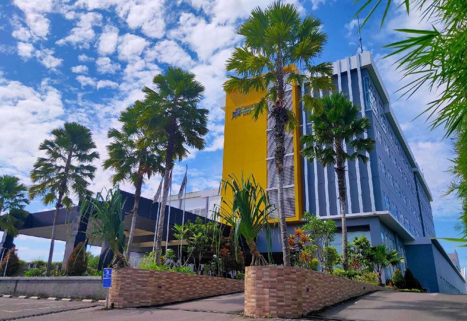 a tall yellow building surrounded by palm trees , with a blue sky in the background at Aquarius Boutique Hotel Sampit