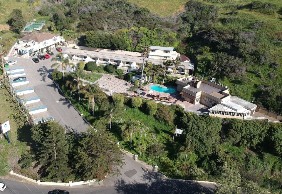 aerial view of a resort with a pool surrounded by palm trees , grass , and buildings at Malibu Country Inn