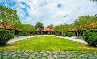 a large , grassy courtyard surrounded by buildings with a red roof and trees in the background at Seava Ho Tram Beach Resort