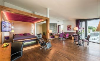 a modern living room with wooden floors , purple walls , and a large bed in the center at Belvoir Swiss Quality Hotel
