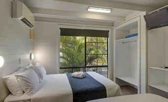 a hotel room with a large bed , white walls , and a window overlooking a tropical garden at Discovery Parks - Ballina