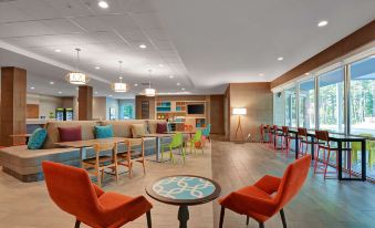 a modern hotel lobby with colorful furniture , including a couch , chairs , and a dining table at Home2 Suites by Hilton Fort Mill